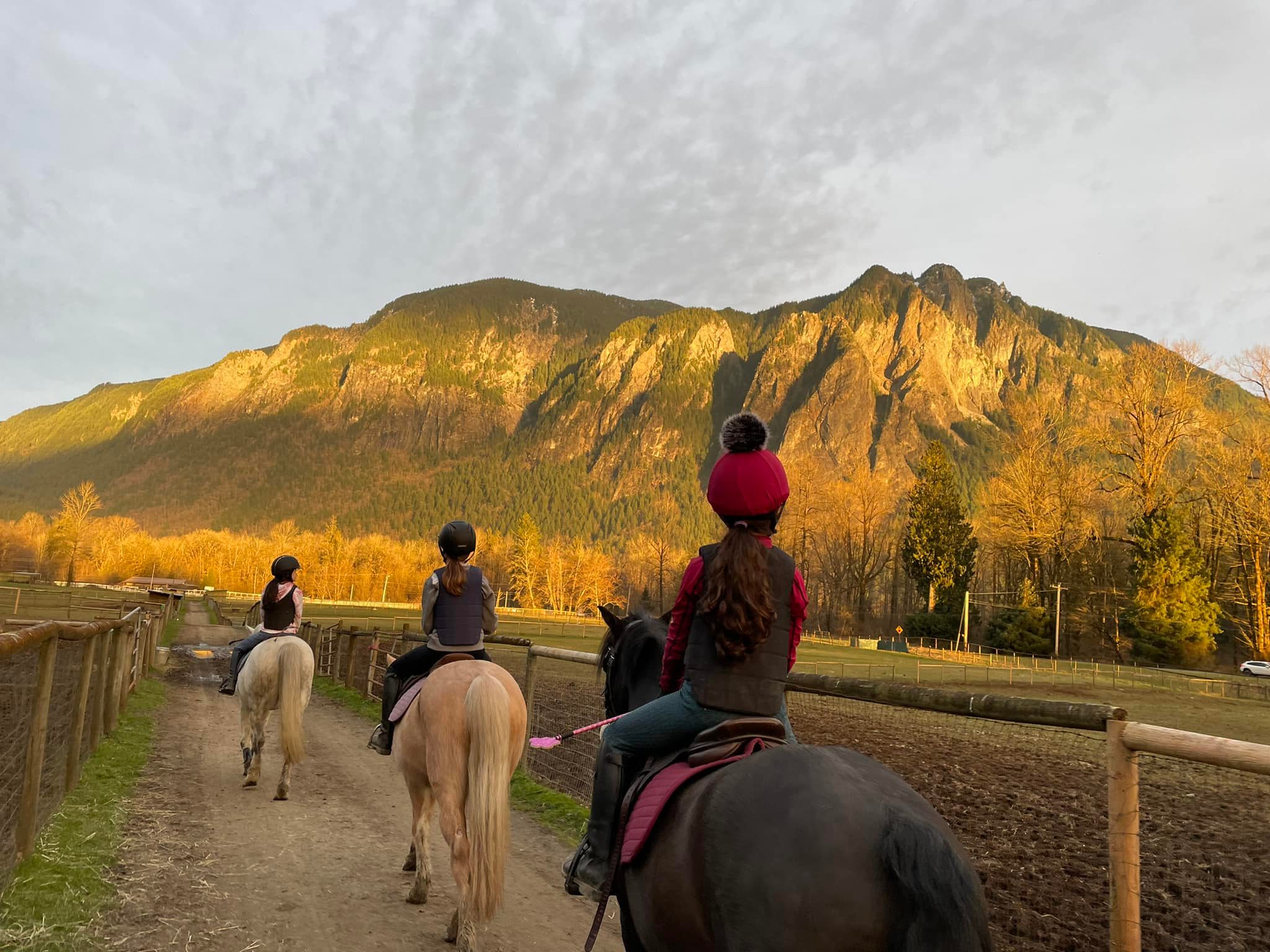Three young riders heading down a trail at sunset with Mt. Si in the background